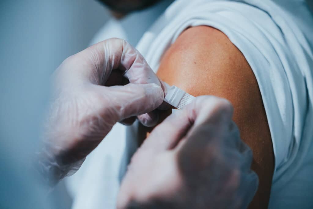 Eine behandschuhte Hand legt einer Person nach einer Injektion einen Verband um den Oberarm, der bei der Bewältigung von Depressionen oder Schmerzen helfen kann.